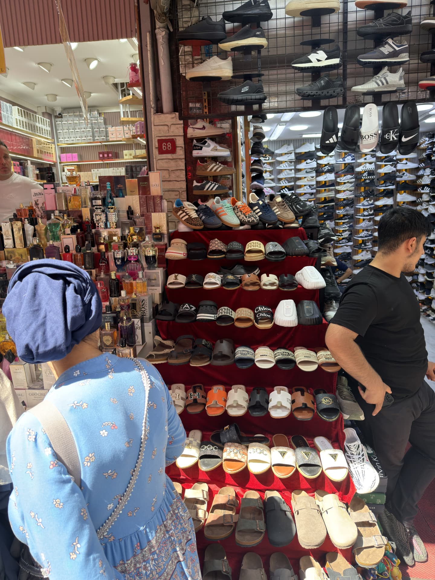 Market display of shoes, perfumes and sandals with shoppers